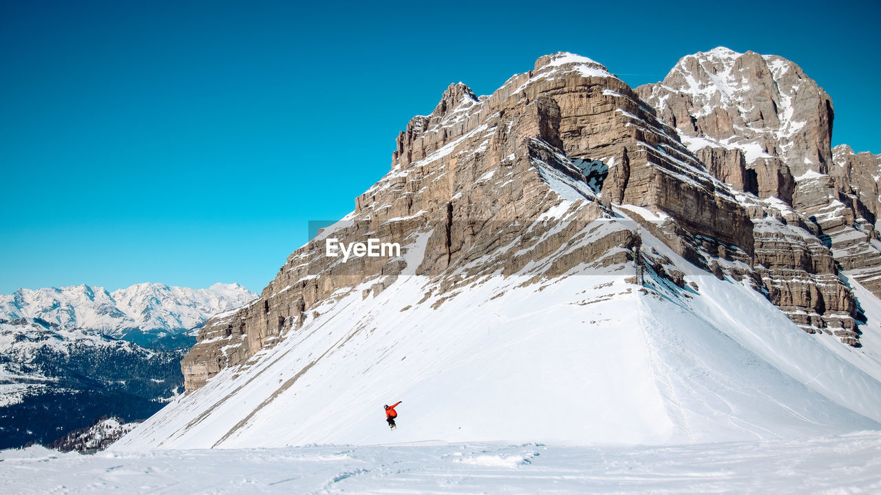 Distant view of person practicing snowboard stunt against dolomites during winter