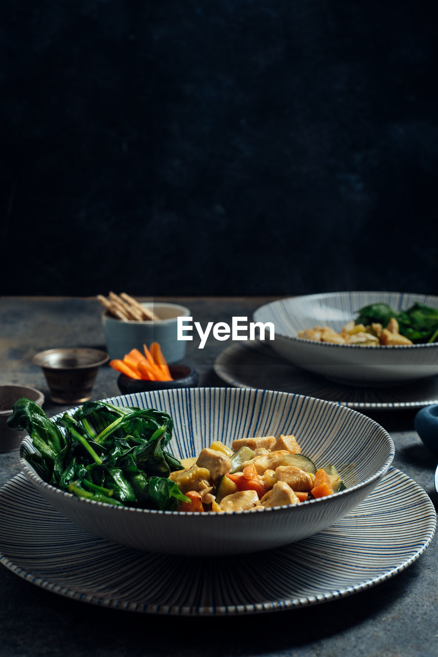 Delicious thai curry coconut chicken, accompanied by tender vegetables and spinach, in a modern blue plate