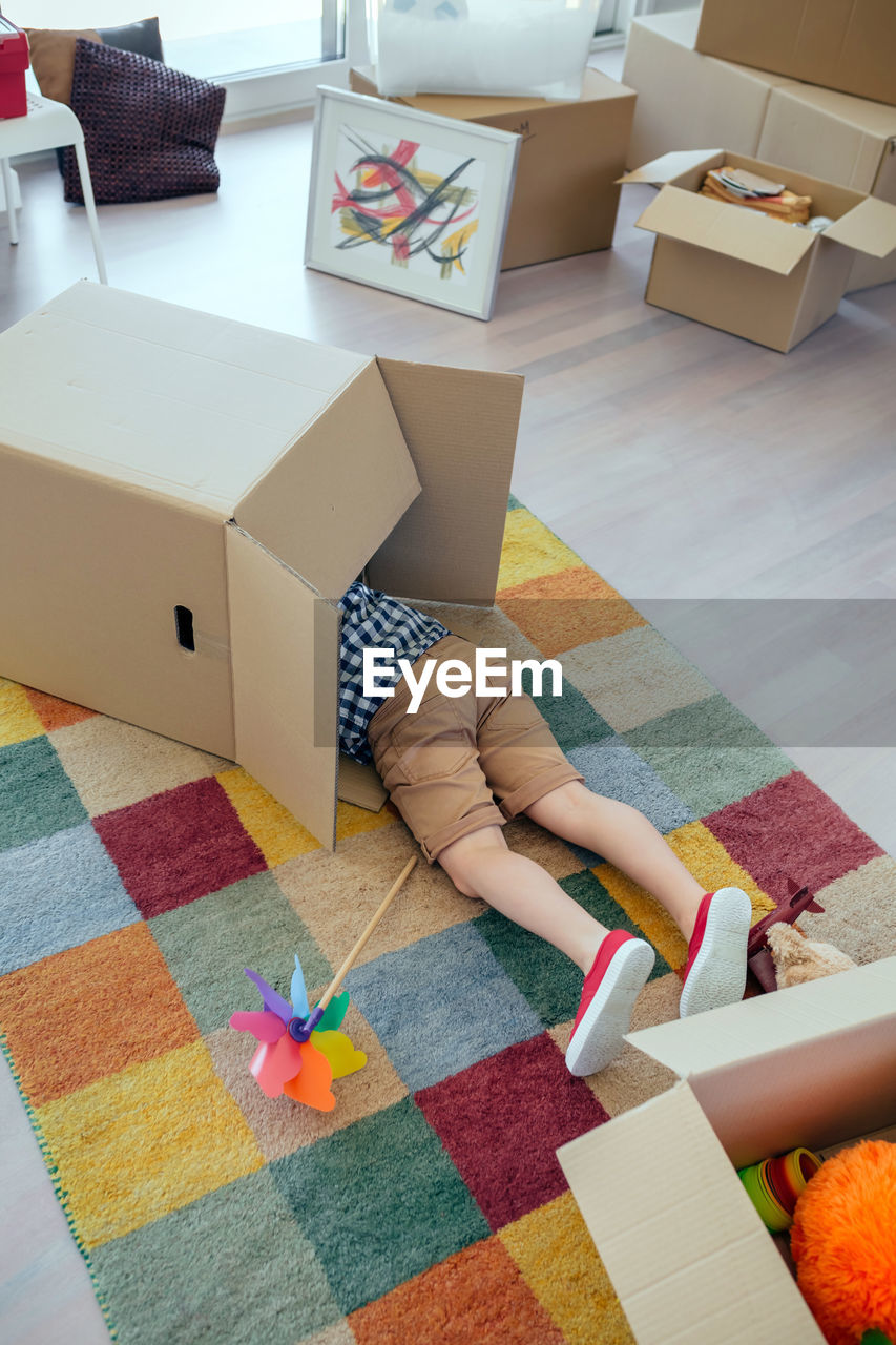 Low section of boy in cardboard box on carpet at home