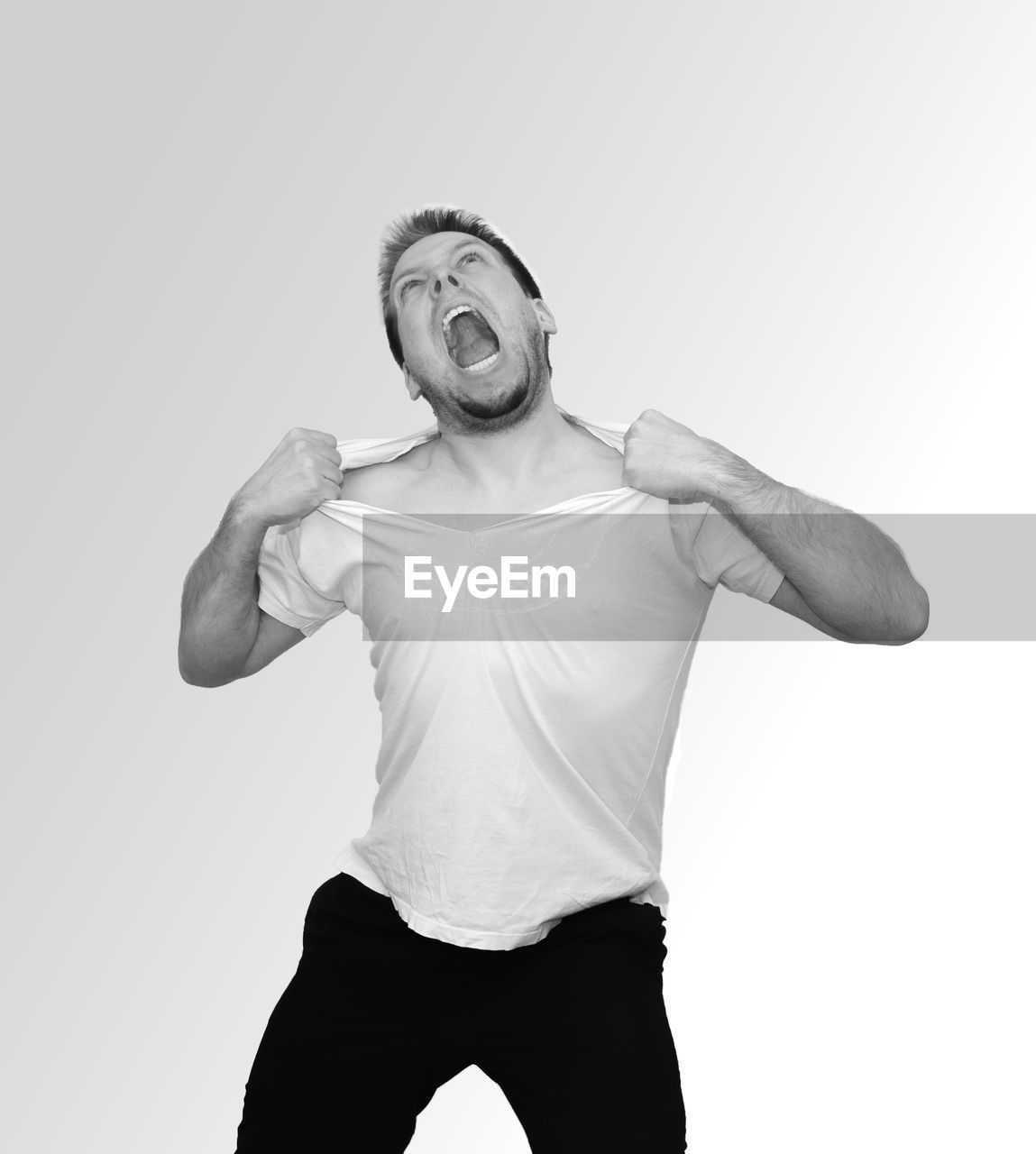 Distraught man tearing t-shirt against white background