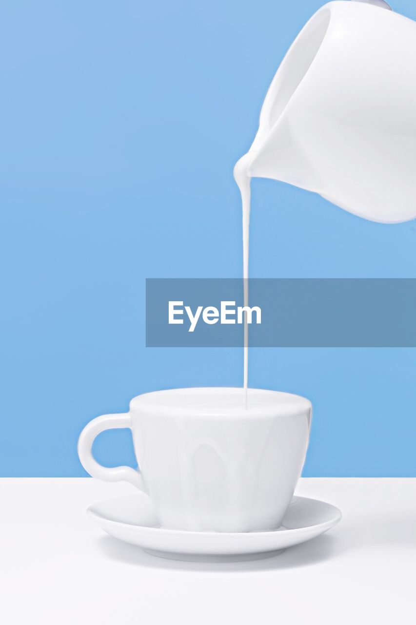 Close-up of jug pouring milk into coffee cup on table