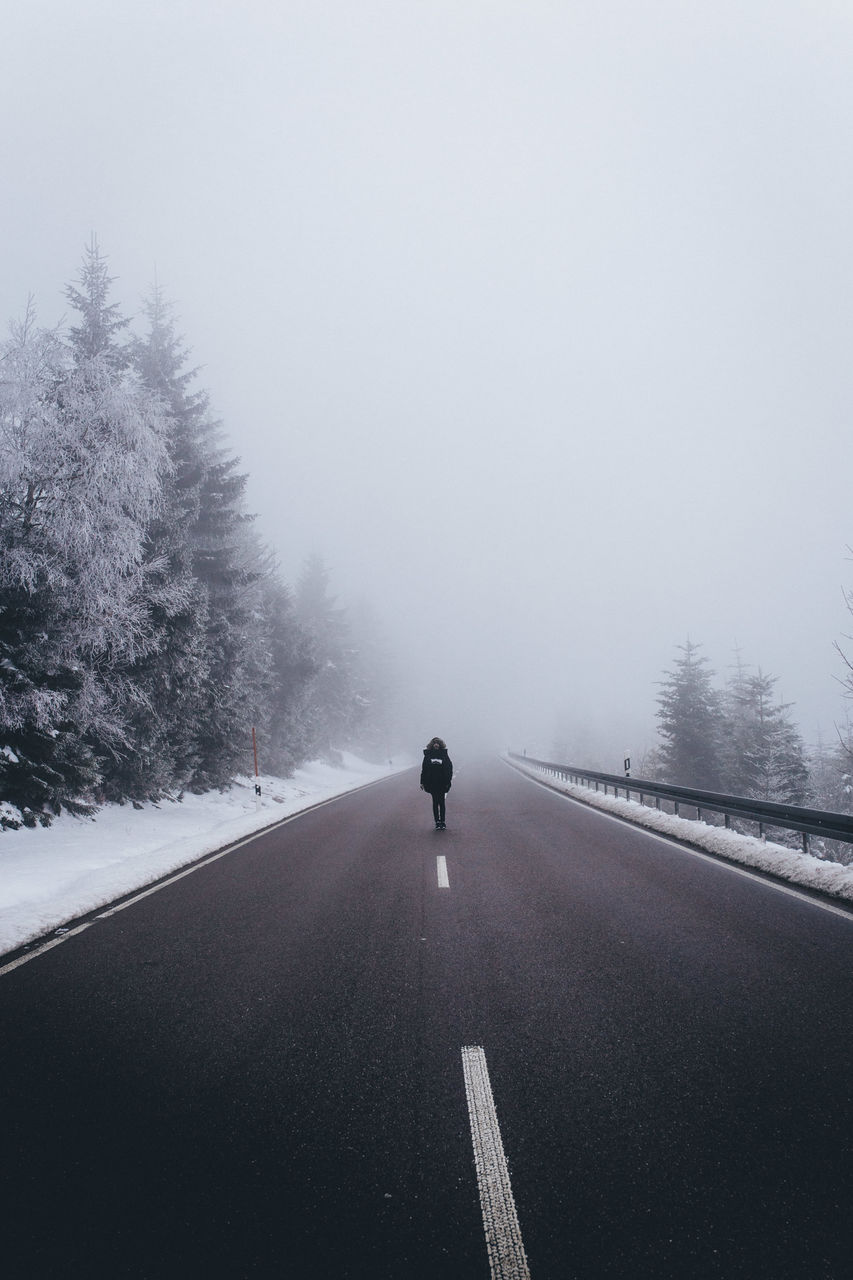 Man walking on road against sky during winter