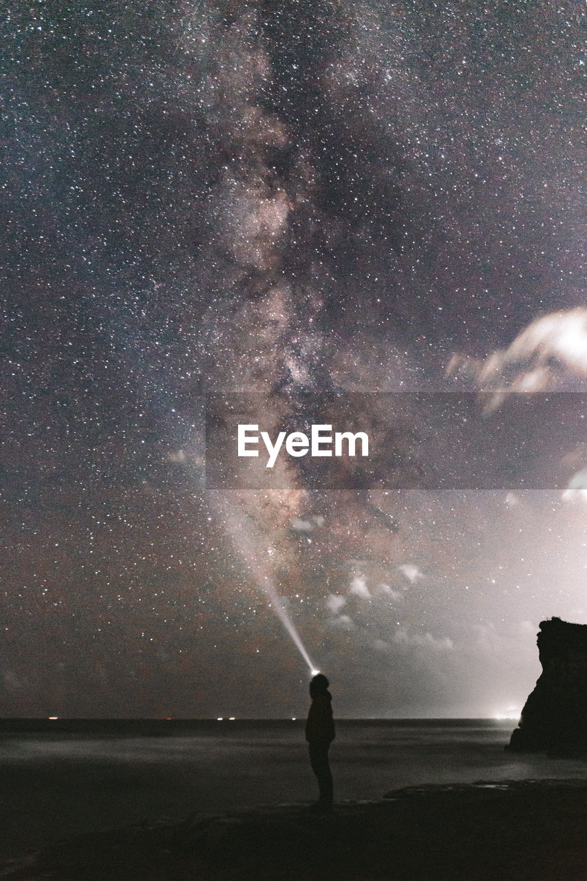 Man standing on beach against sky at night