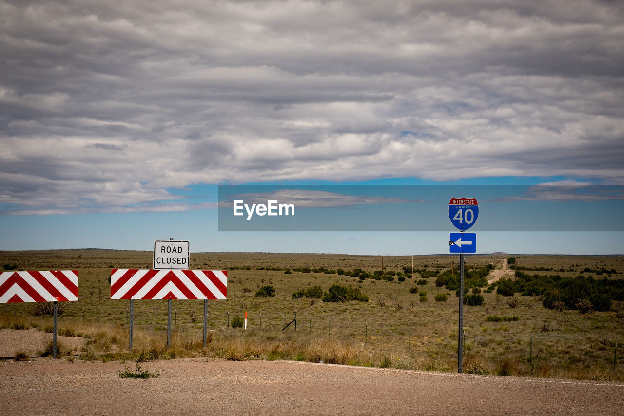 Road signs on landscape against cloudy sky