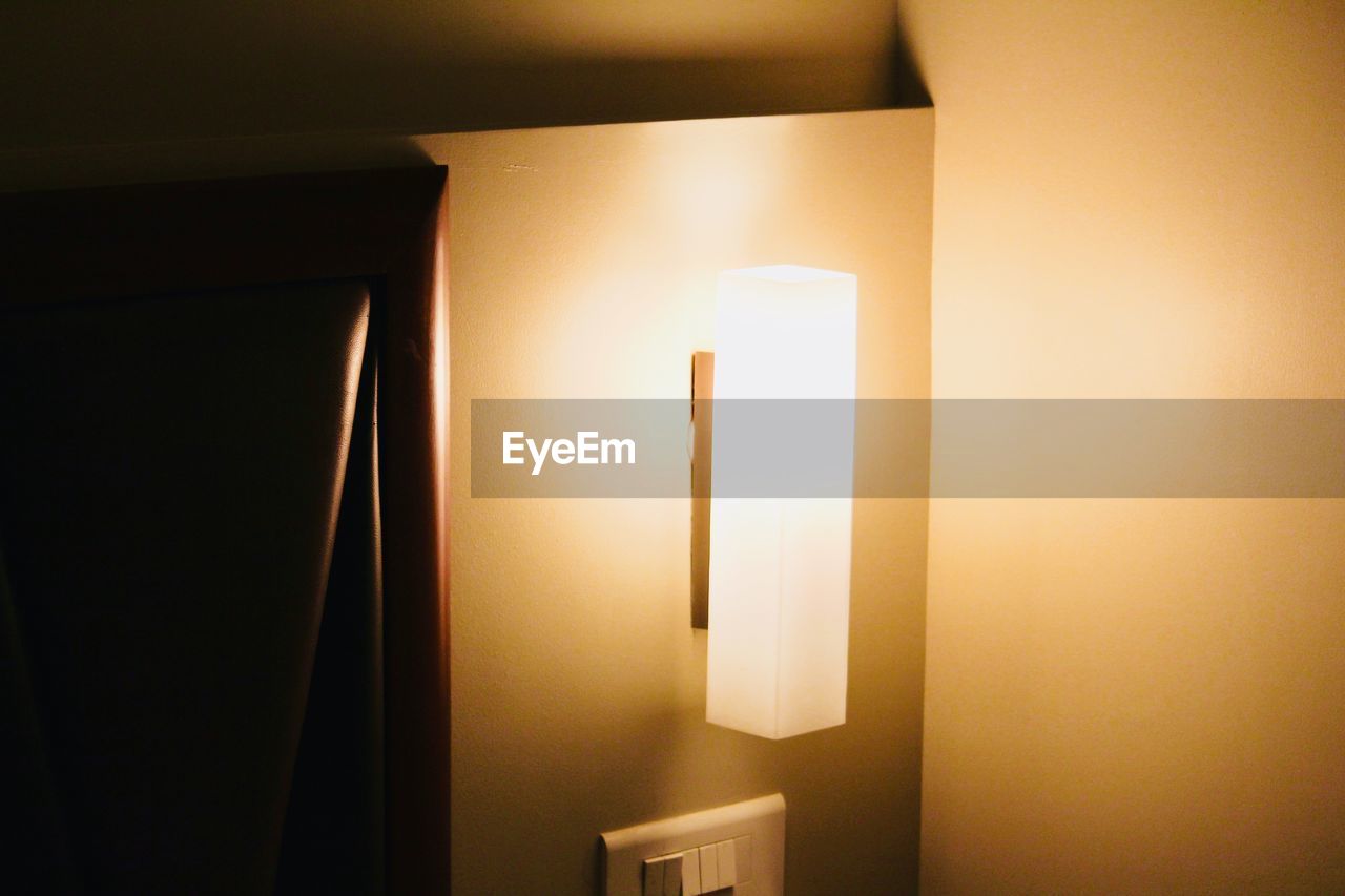 CLOSE-UP OF ILLUMINATED LAMP AGAINST WALL AT HOME