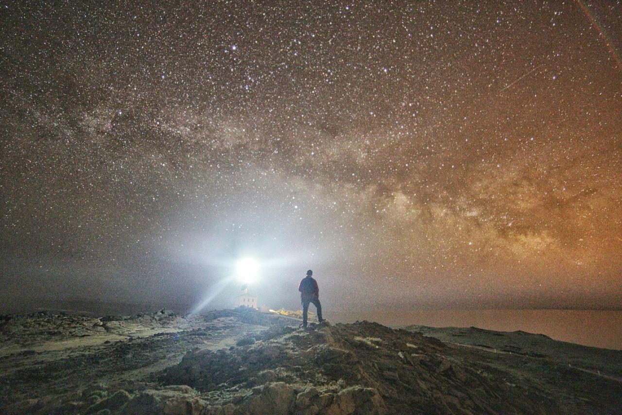 Rear view of man standing against glittering sky at night