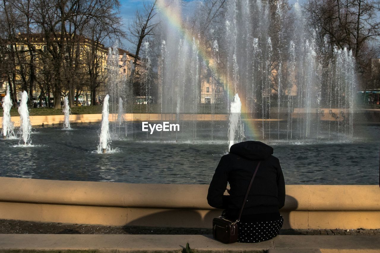 Rear view of woman sitting by fountain in park