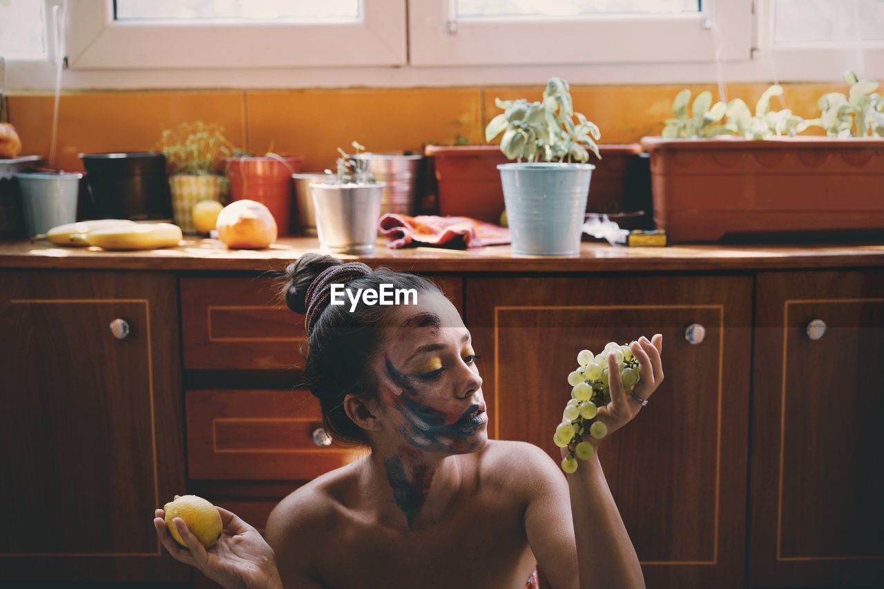 Woman with face paint holding fruits in kitchen