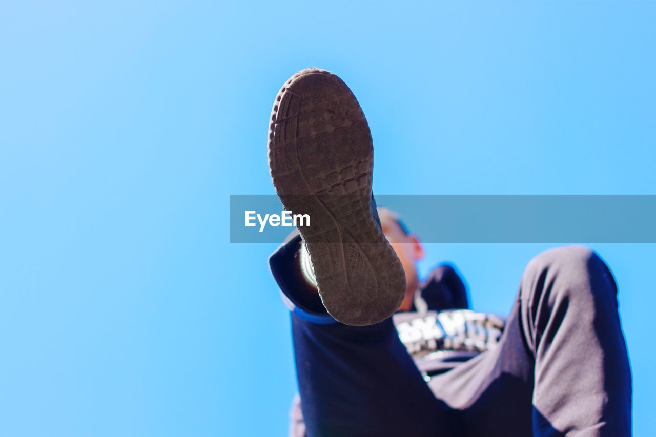 Low angle view of man wearing shoe against clear blue sky
