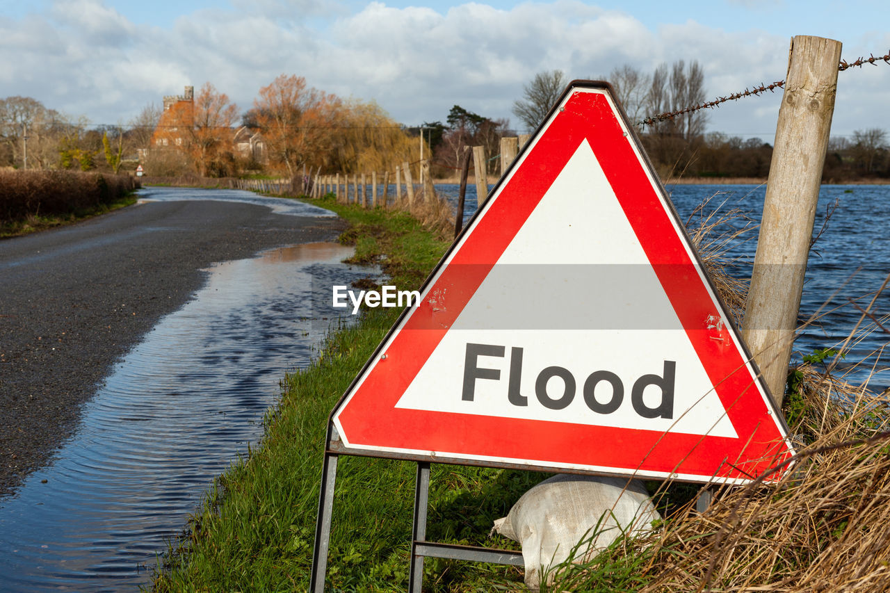 Flood triangular warning sign on road flooded by river that has burst is banks with selective focus 