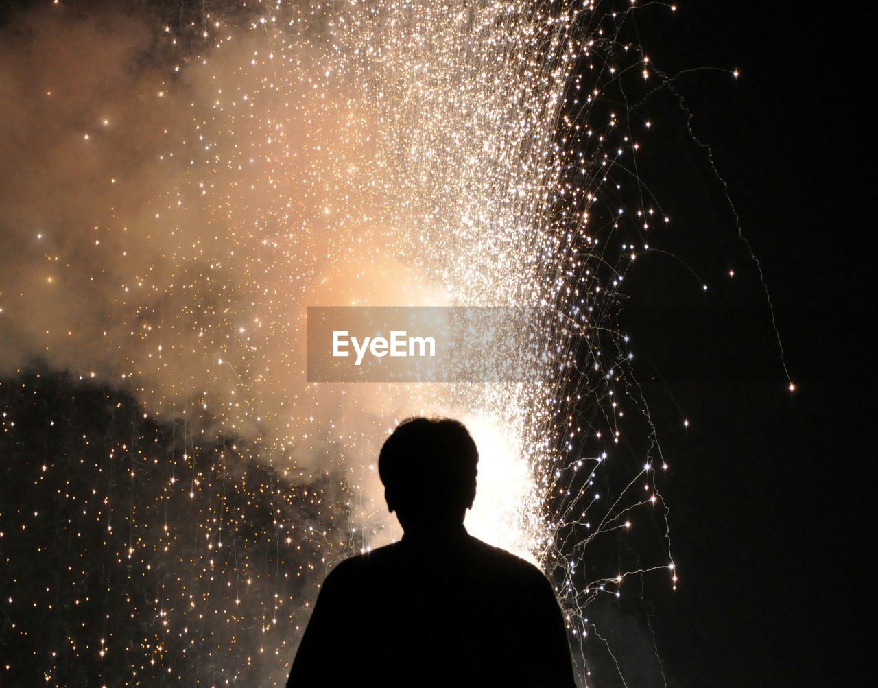 Rear view of silhouette man looking at firework against sky