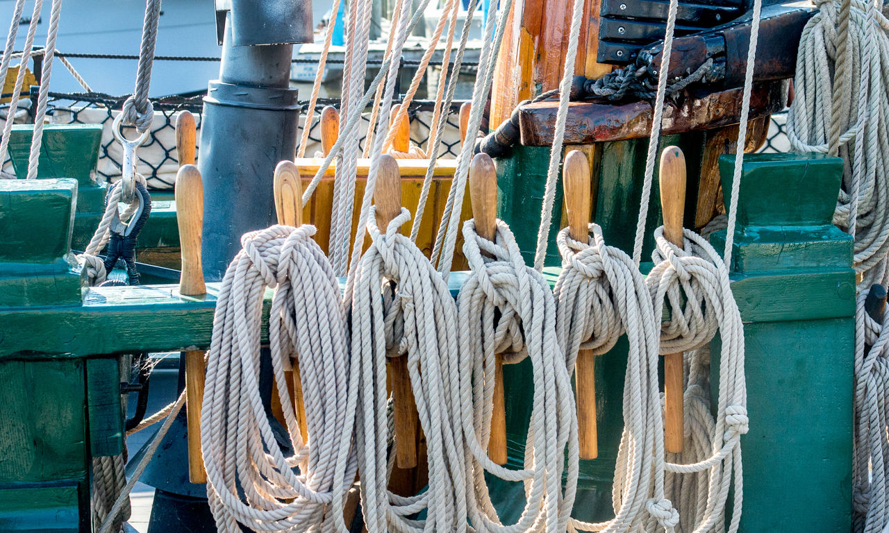 Ropes from sails on a antique tall ship, are neatly tied along wood posts 
