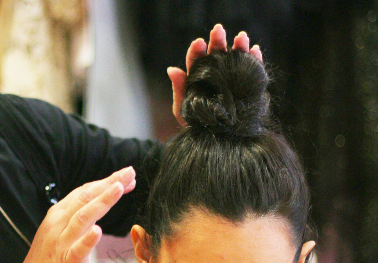 Cropped image of hairdresser hands making hair bun of woman
