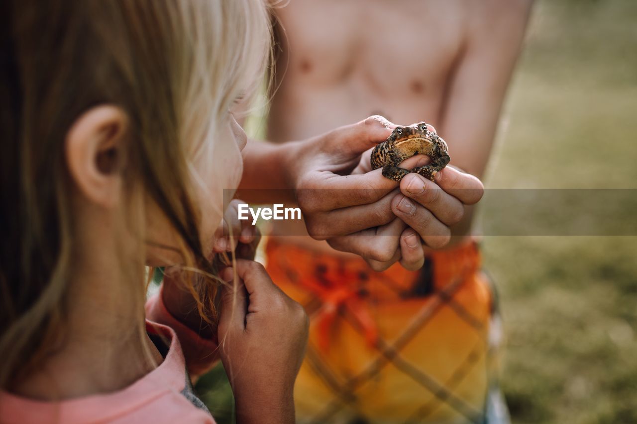 Girl by shirtless boy holding frog