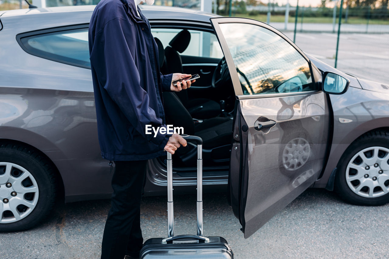 Man standing with luggage by car parked in city