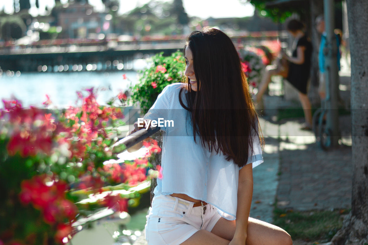 Smiling young woman looking away while sitting by plants in park