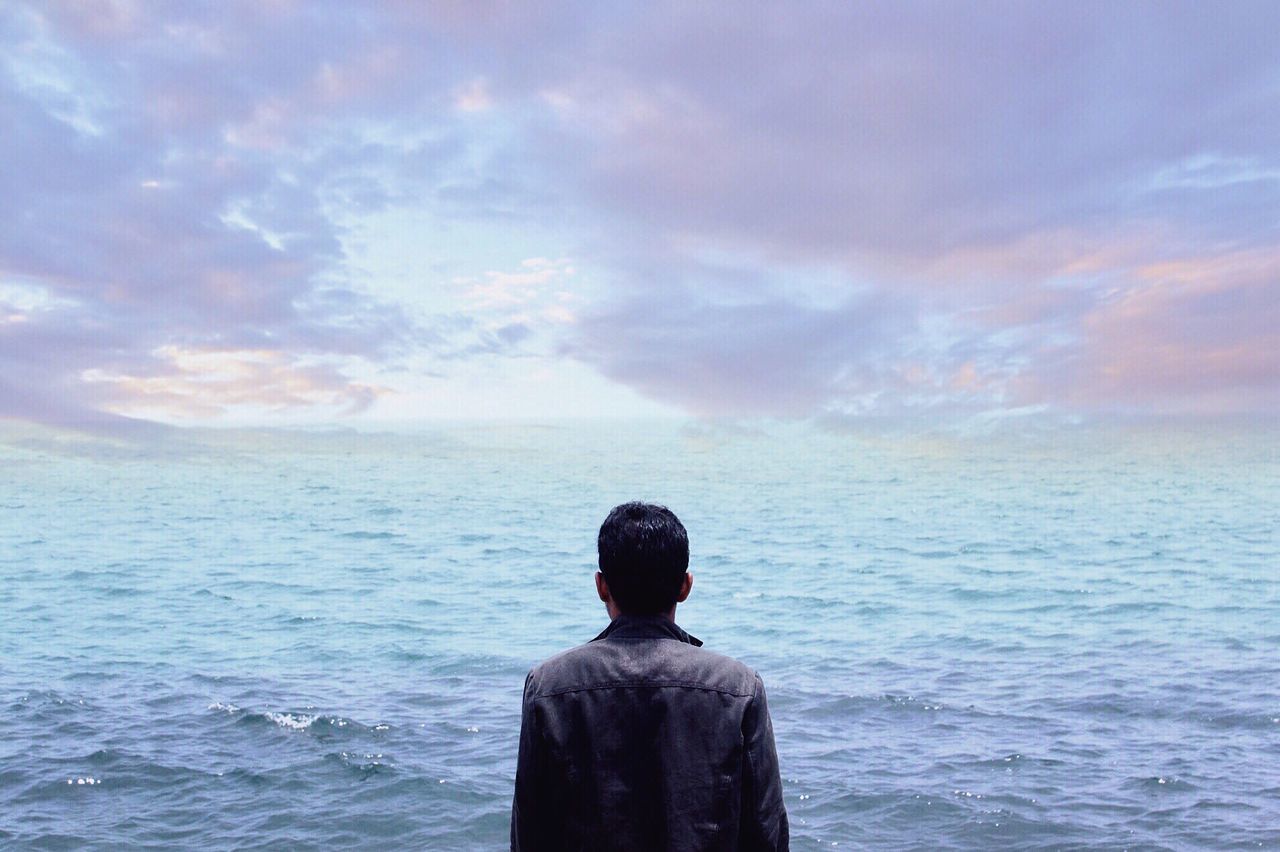 Rear view of man standing in front of sea against cloudy sky