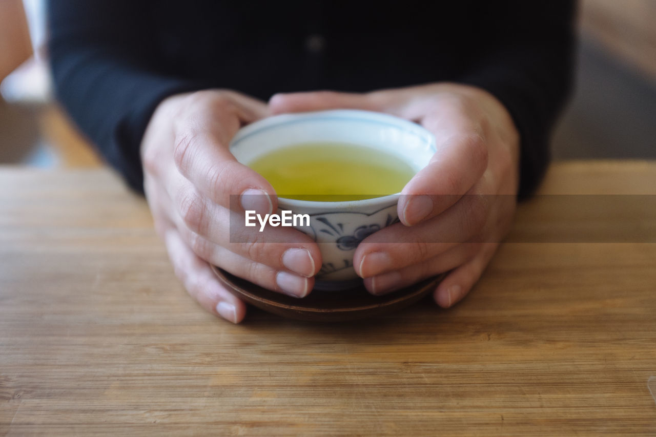 Close-up of person holding green tea on wooden table