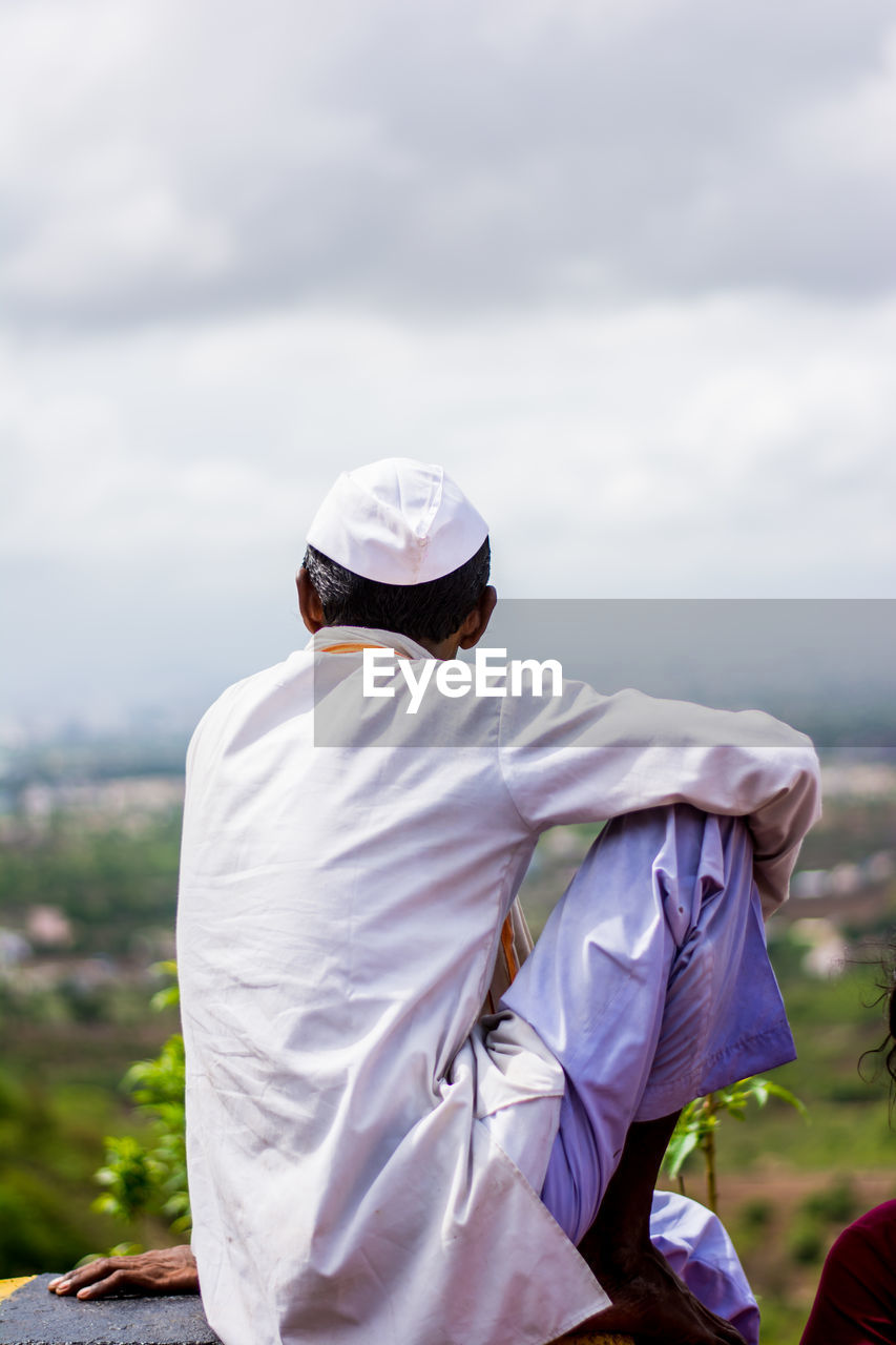 Rear view of man wearing topi looking at field