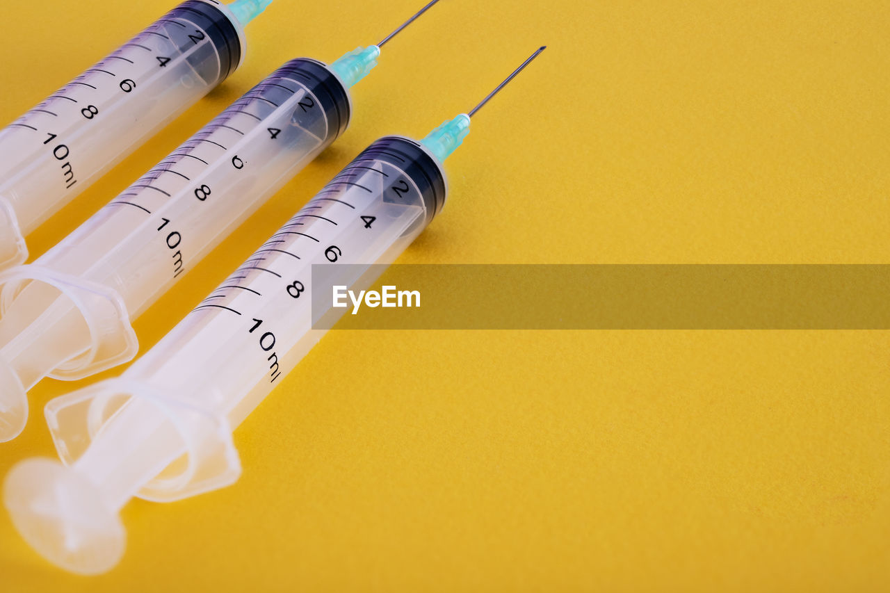 High angle view of syringes on yellow background