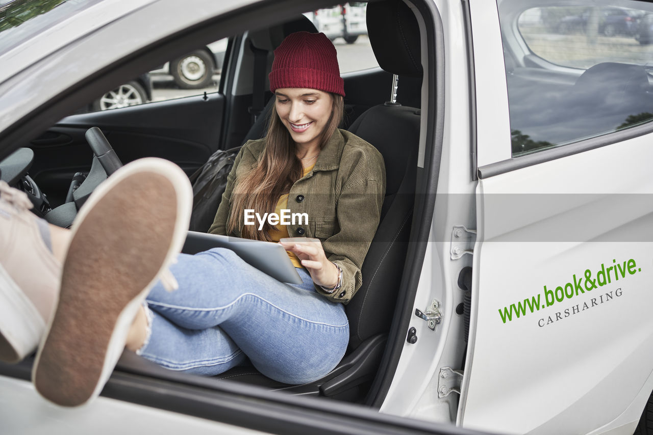 Smiling young woman using digital tablet while sitting in car