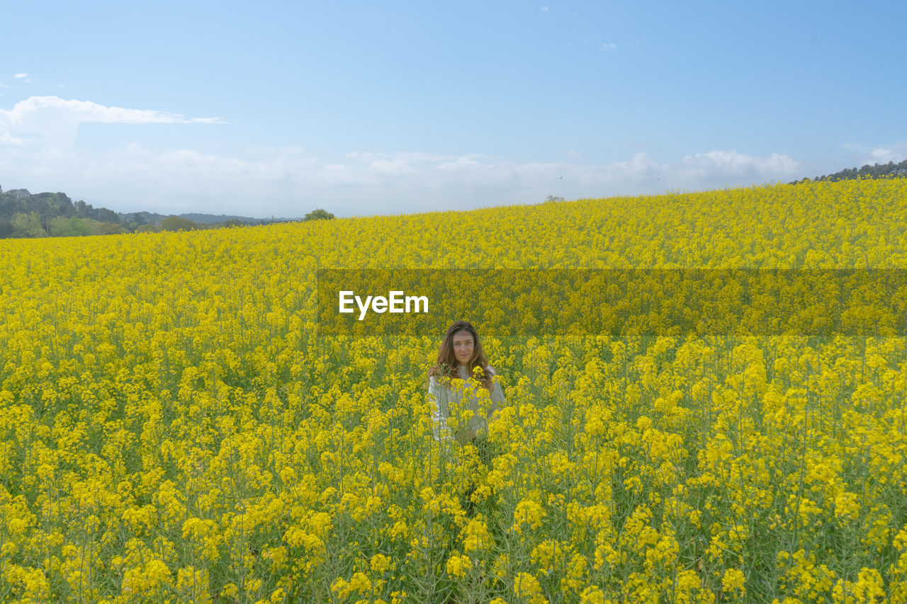 Scenic view of oilseed rape field against sky and a girl in the middle