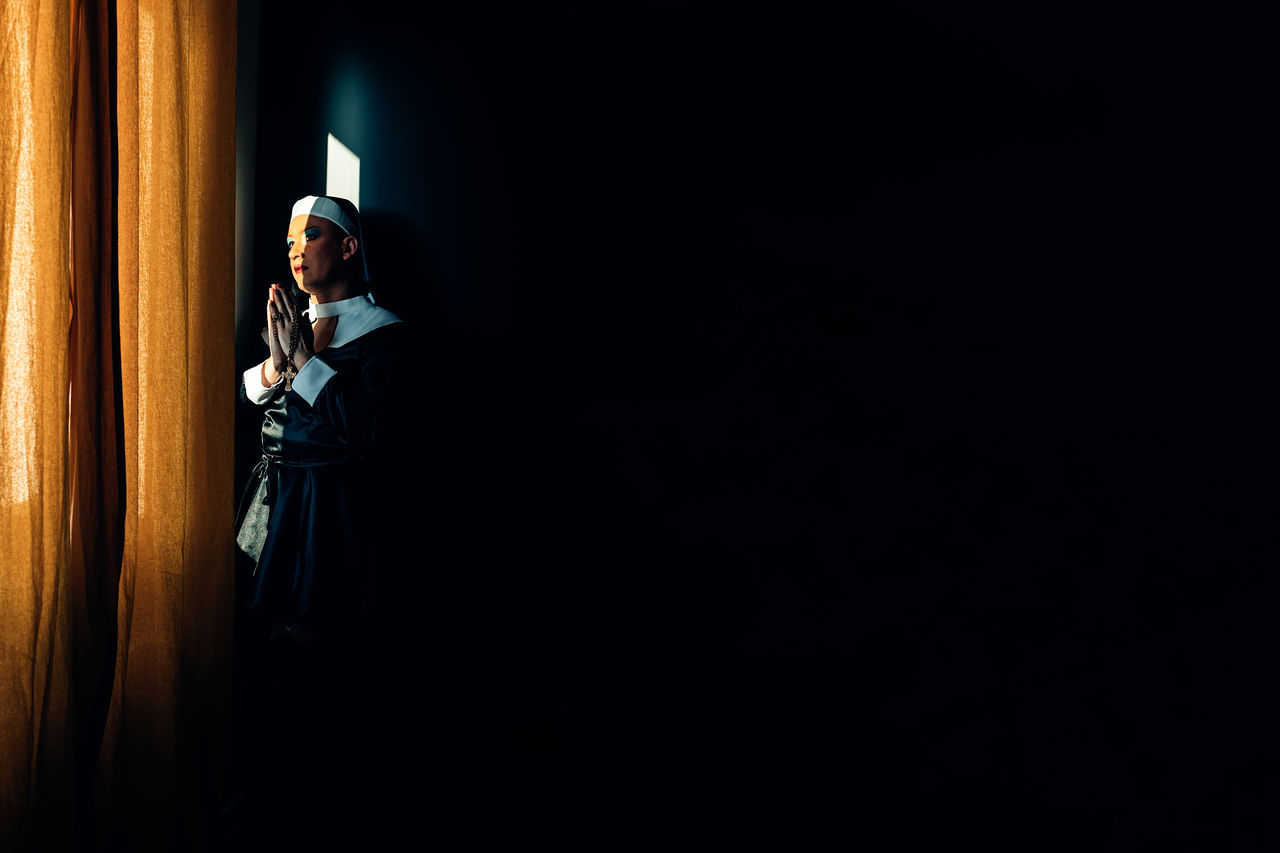 Devoted nun prays in the light of a convent window. cross dressing drag queen, religion, identity.