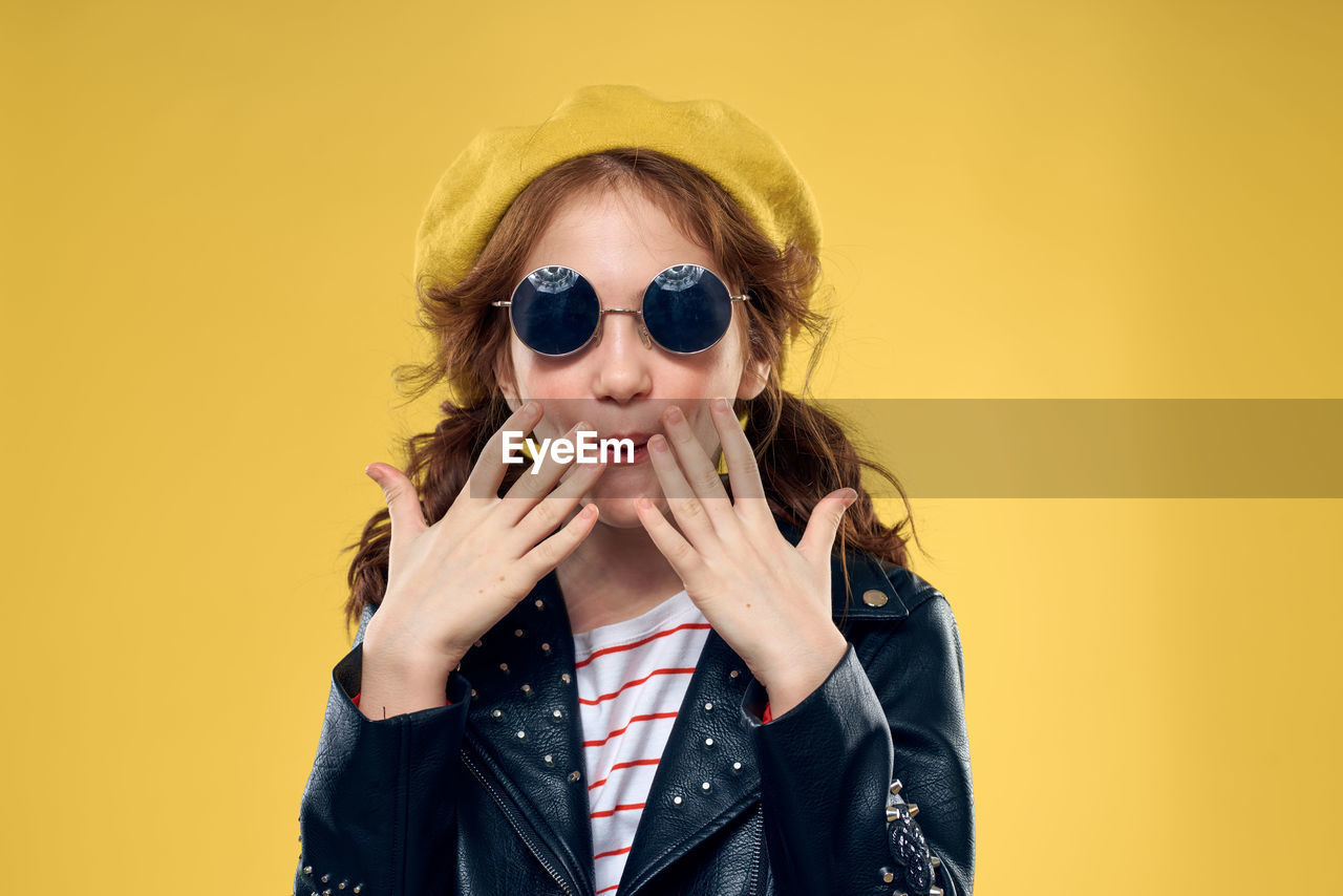 portrait of young woman wearing sunglasses against yellow background