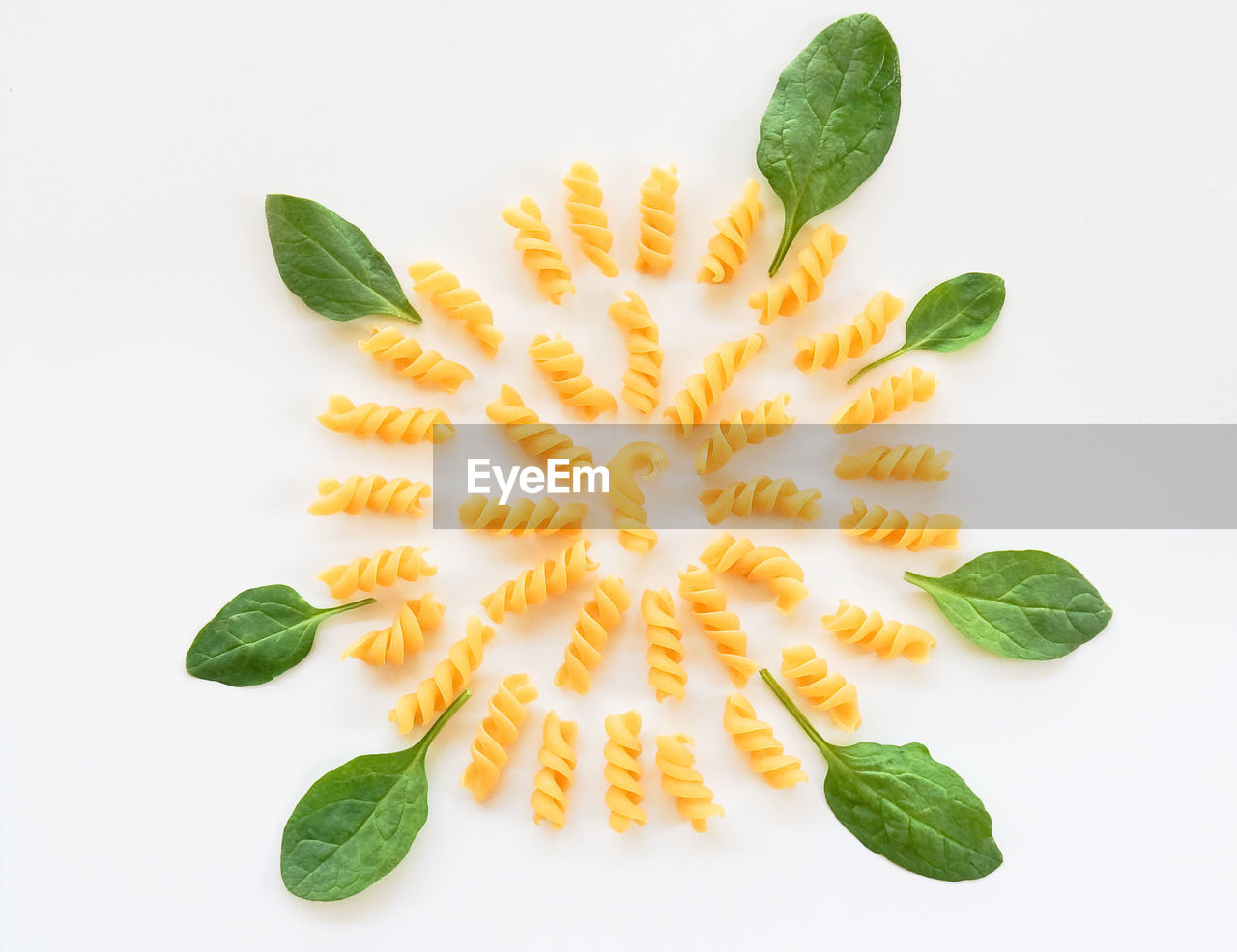 Twisted raw pasta and spinach leaves circle shape food knolling white background 