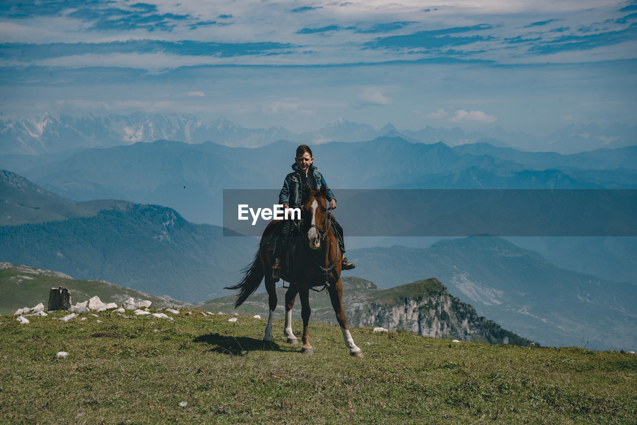 Full length of boy sitting on horse against mountain