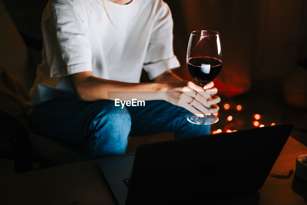 Young woman having video call on laptop computer and drinking wine.