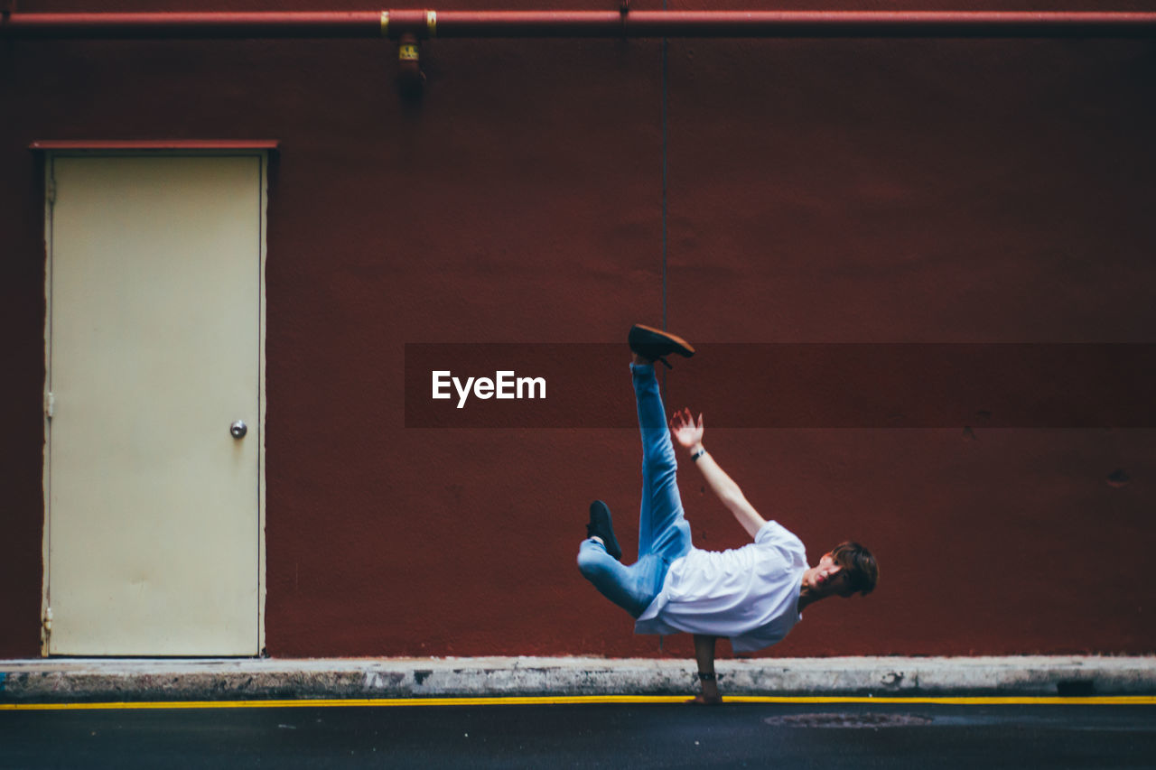 Full length of male dancer breakdancing on street by maroon wall