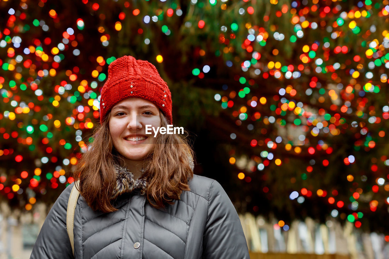Portrait of smiling girl wearing hat against illuminated lights