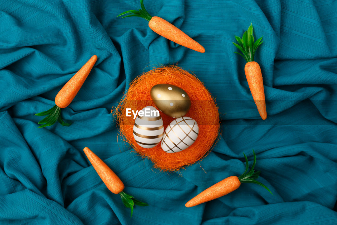 Minimal layout of golden easter egg in orange nest with bunny carrot circling around cyan background
