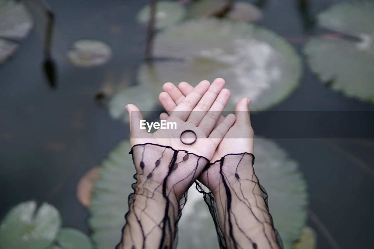 Cropped hands of woman holding ring over lotus leaves in lake