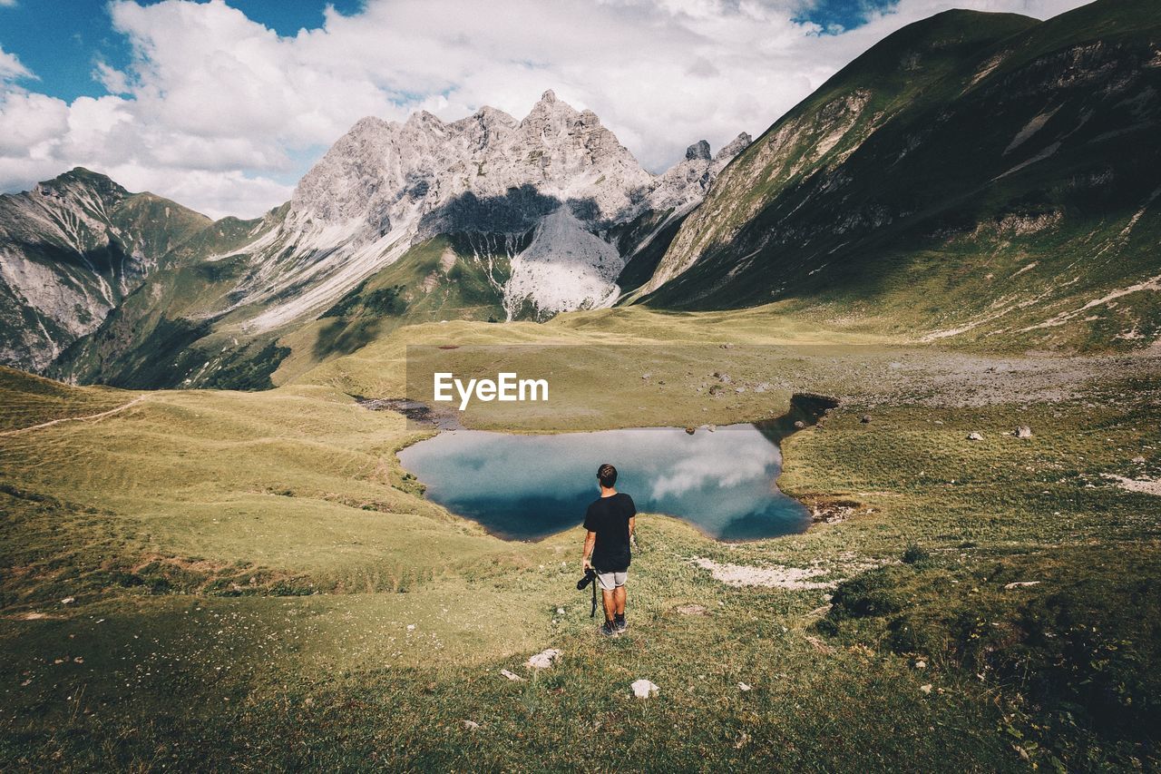 Rear view of man standing on field against mountains