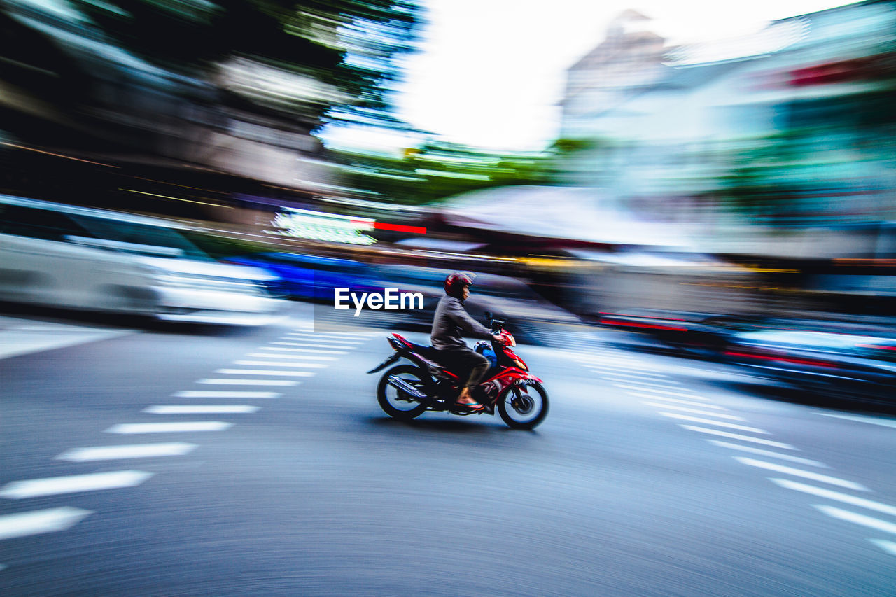 Person riding bike on road with blurred motion of city in background