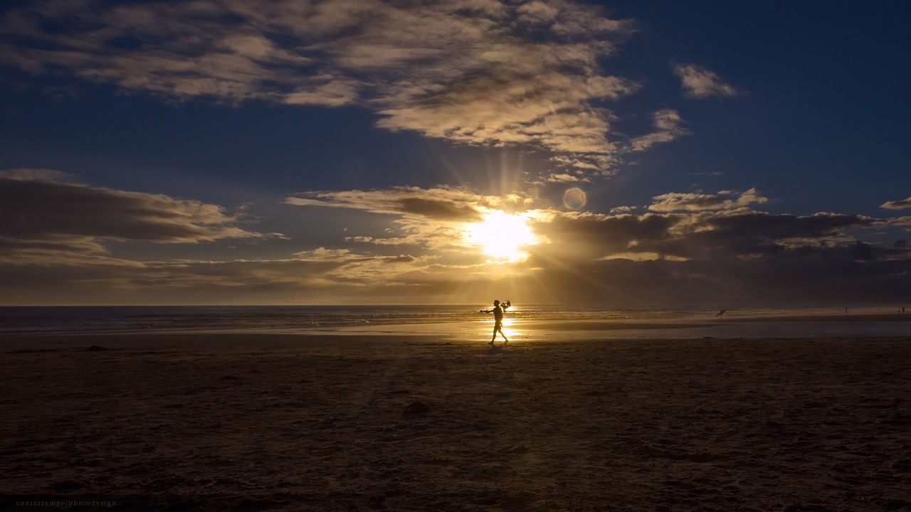 Silhouette person walking on shore at beach against sky during sunset