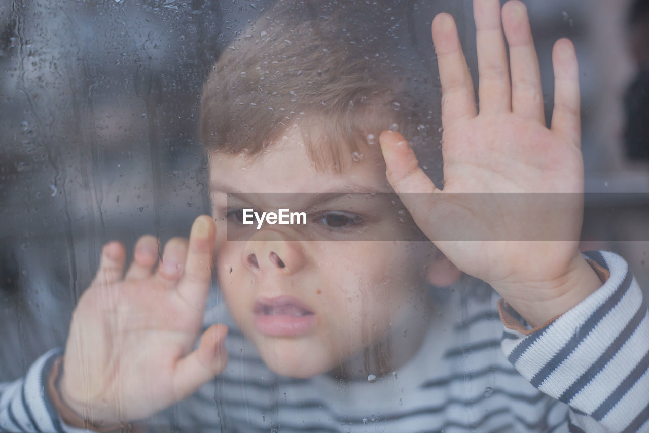 Close-up of boy looking through wet window during rainfall