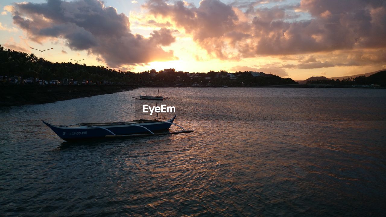 Outrigger boat in river against cloudy sky at dusk