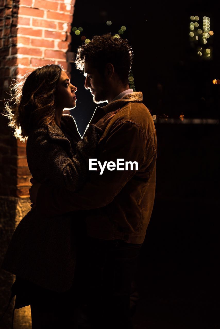 Young couple embracing while standing outdoors at night