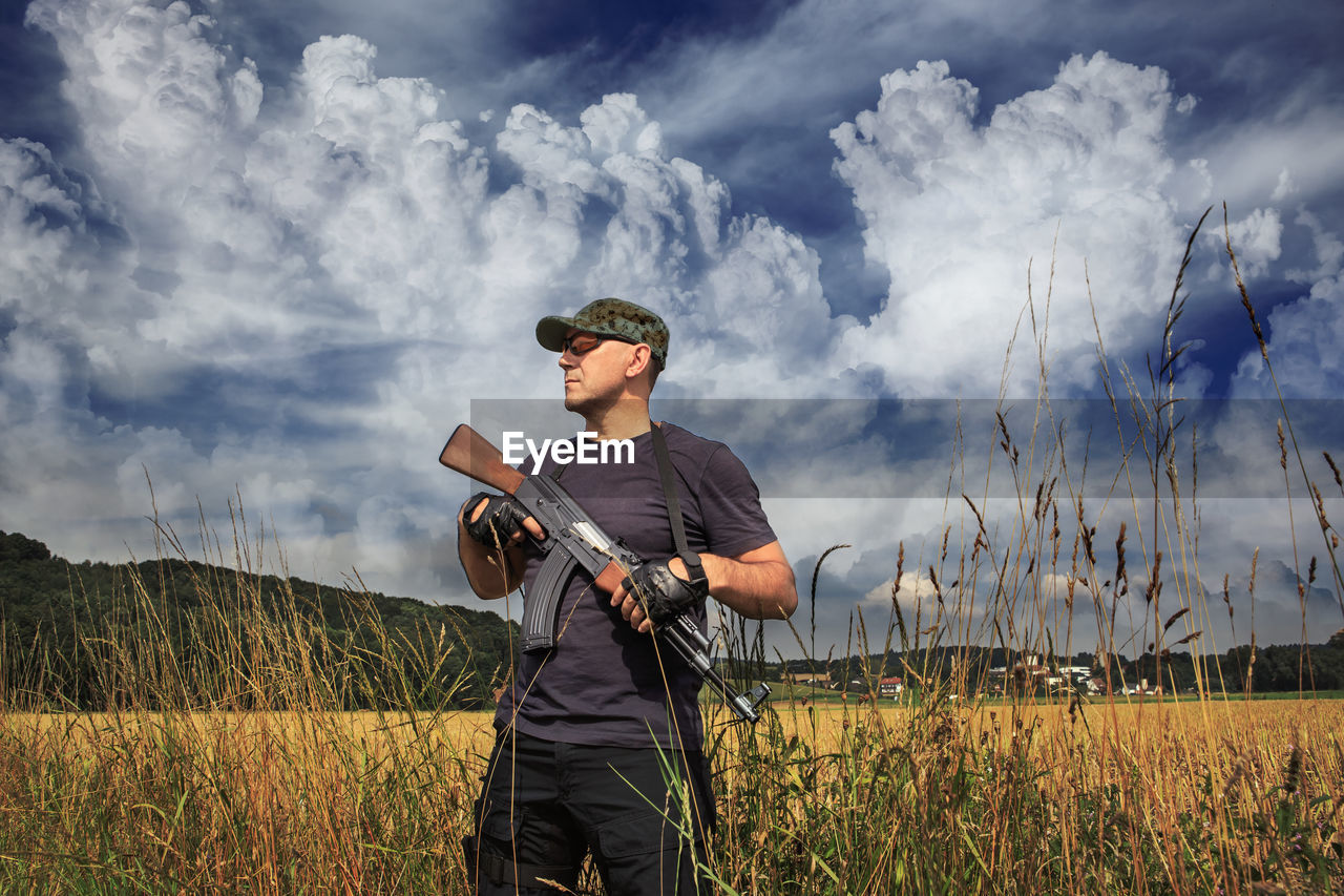 Man holding rifle standing against sky
