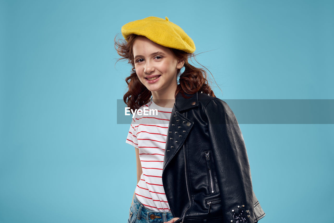 portrait of young woman wearing hat standing against blue background