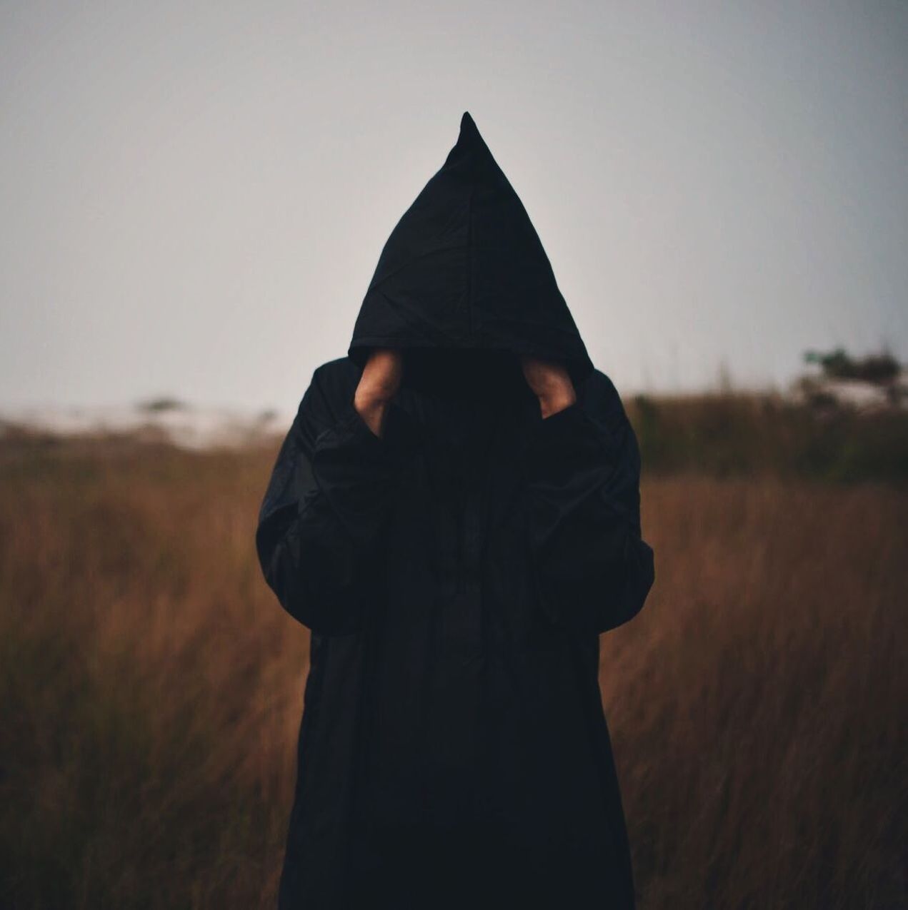 Man wearing hooded jacket hiding face while standing at field