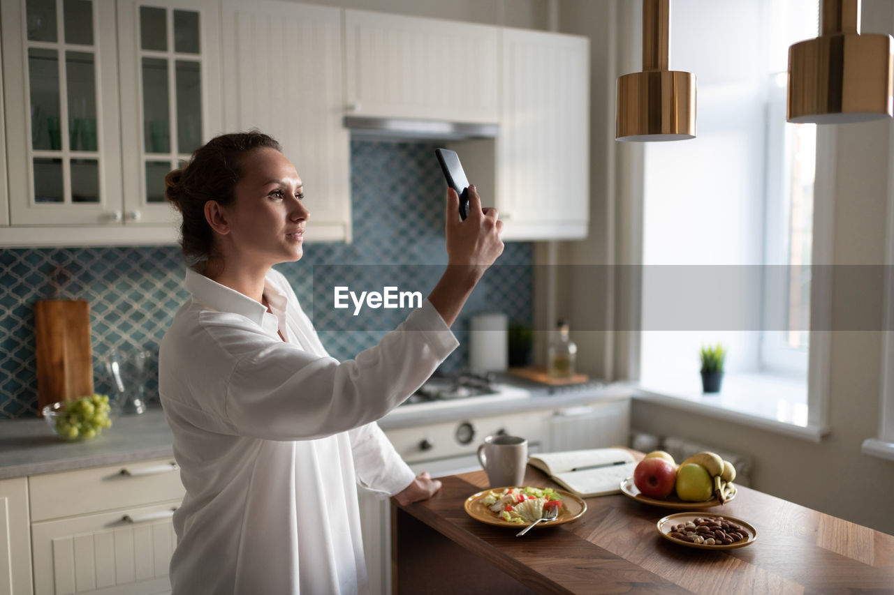 Businesswoman using smartphone for communication in kitchen