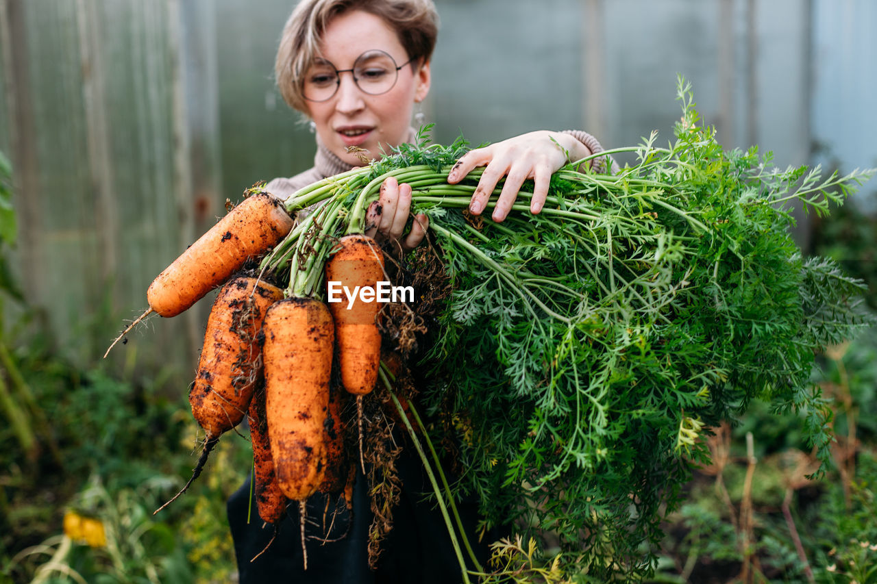 Smiling woman holding carrots at farm