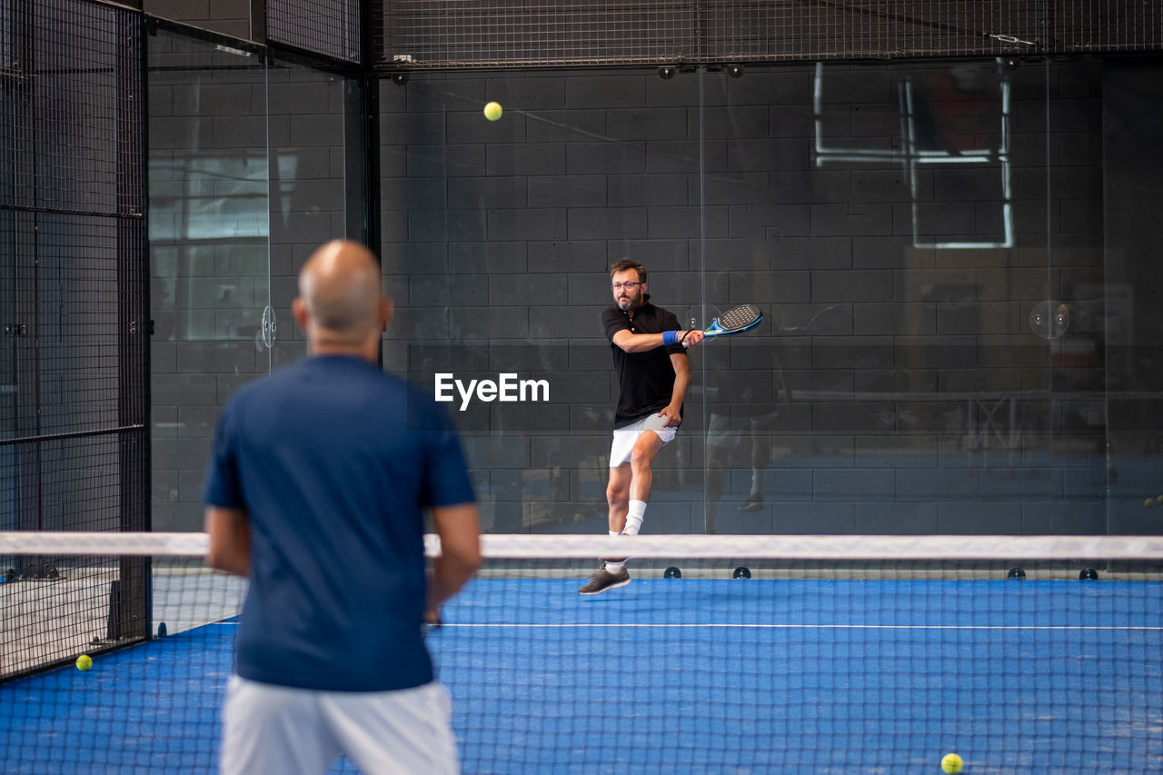 Monitor teaching padel class to man, his student - trainer teaches boy how to play padel on indoor 