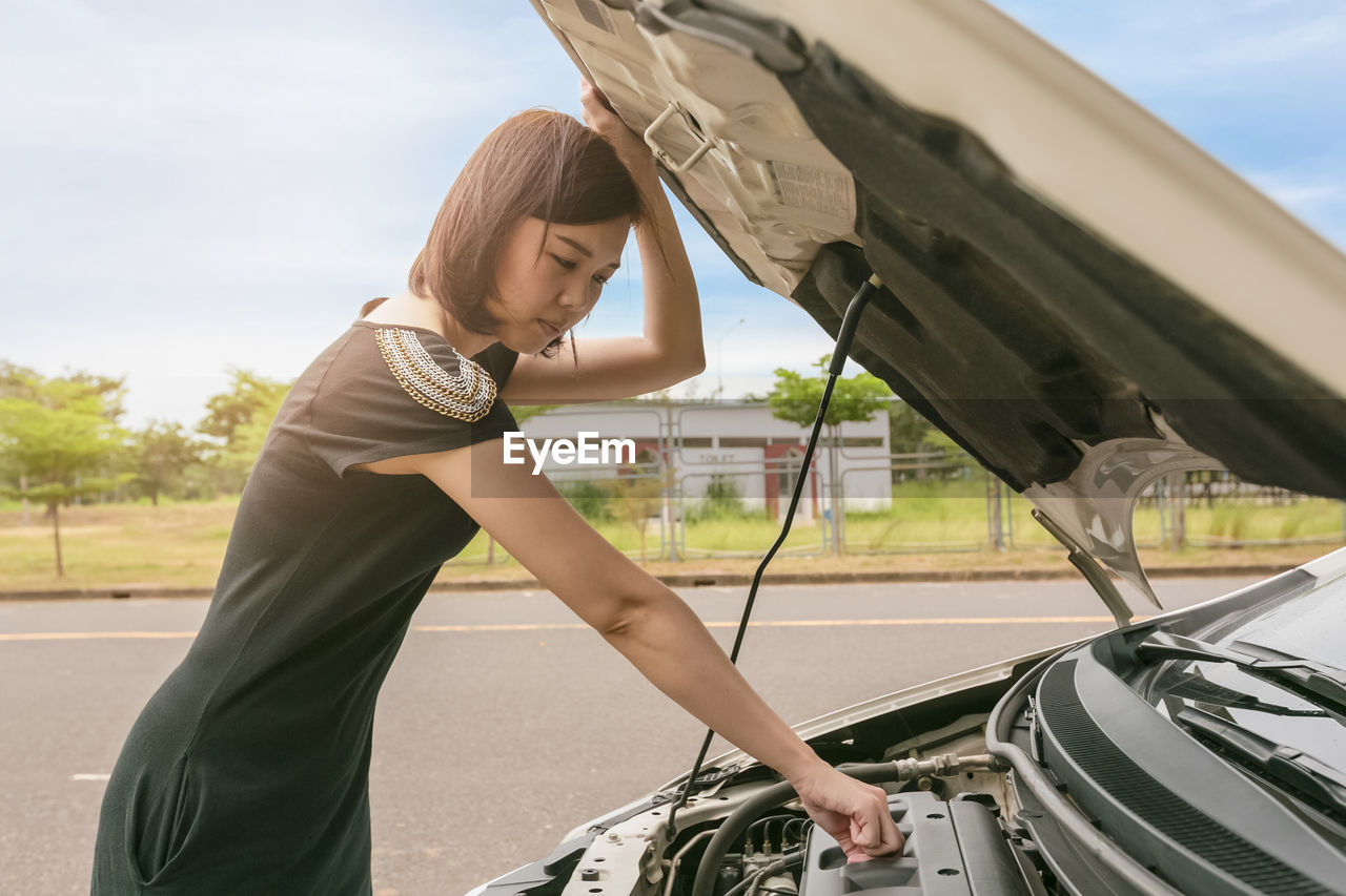 Side view of woman checking car engine on road