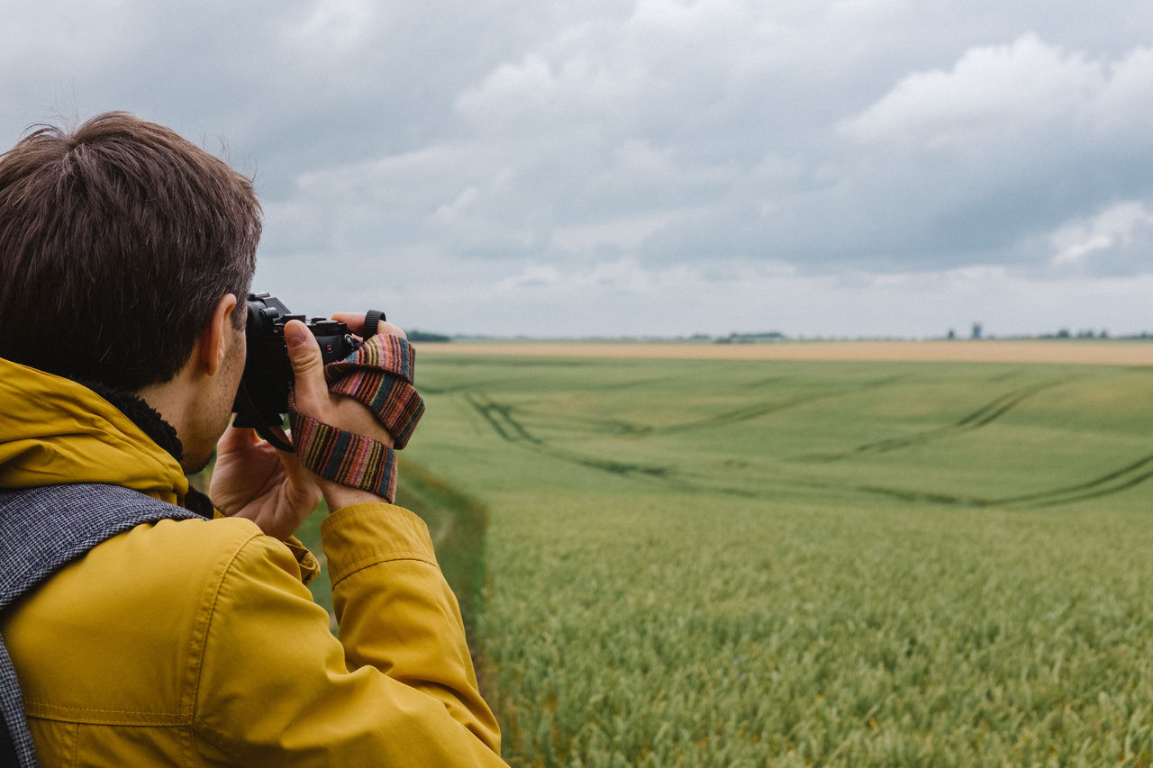 Man photographing agricultural field against sky
