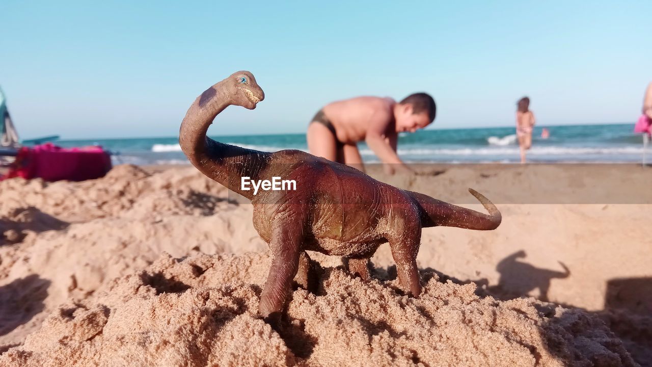 Toy dinosaur at beach against clear sky